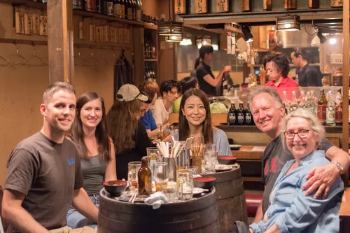 Small group of travelers sharing a meal at a barrel table during an izakaya dinner in Japan