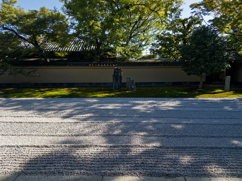 A raked-gravel Zen garden with standing stones behind a temple wall in Kyoto