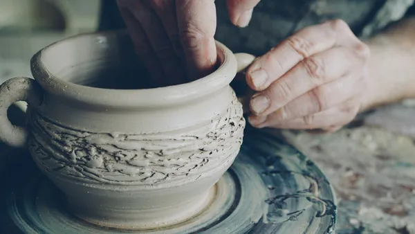 A craftsperson's hands shaping wet clay on a potter's wheel during a craft workshop in Japan