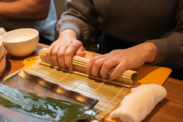 Hands rolling sushi with a bamboo mat during a hands-on sushi-making experience in Japan